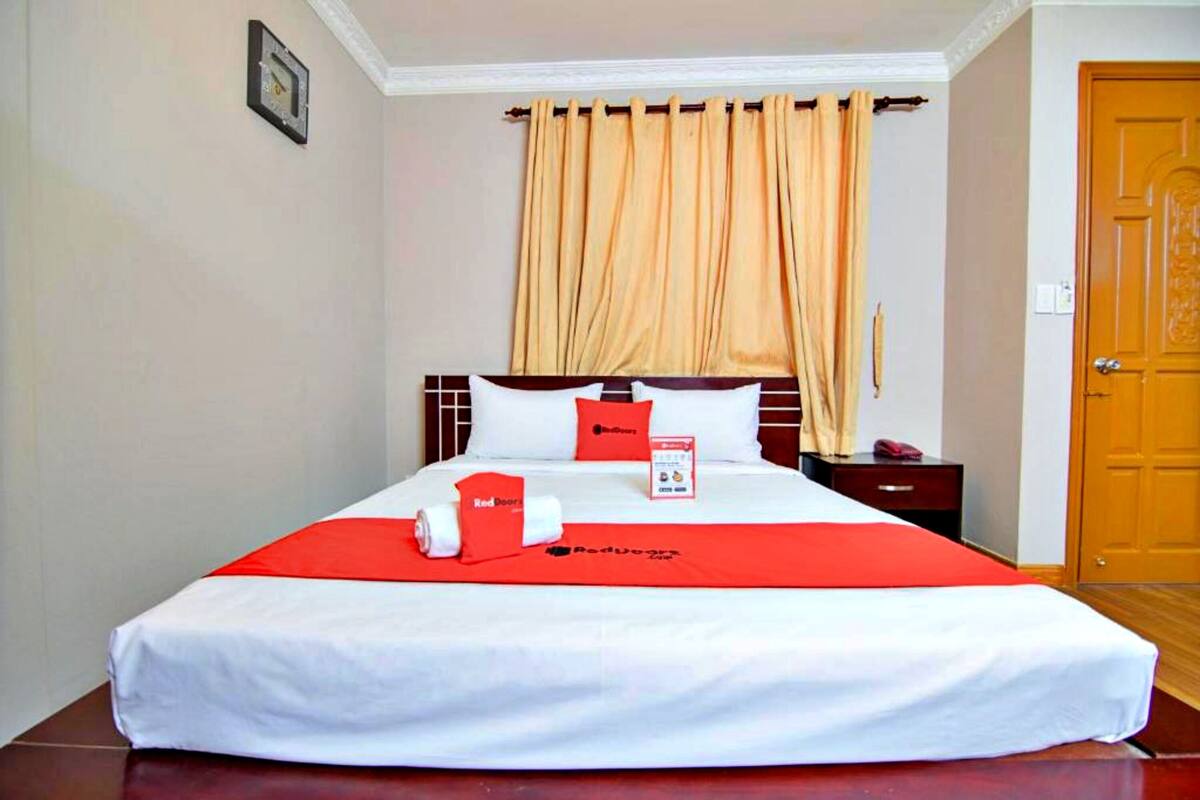 A hotel room with a bed, a nightstand, a red and white bedspread, and a wooden door.