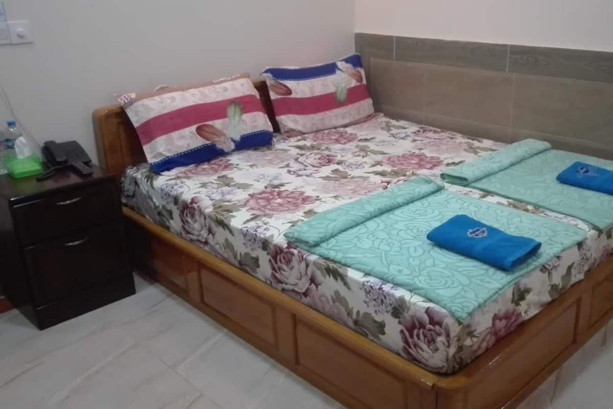 A neatly made bed with floral bedding, a wooden headboard, and a bedside table with a phone and a bottle.
