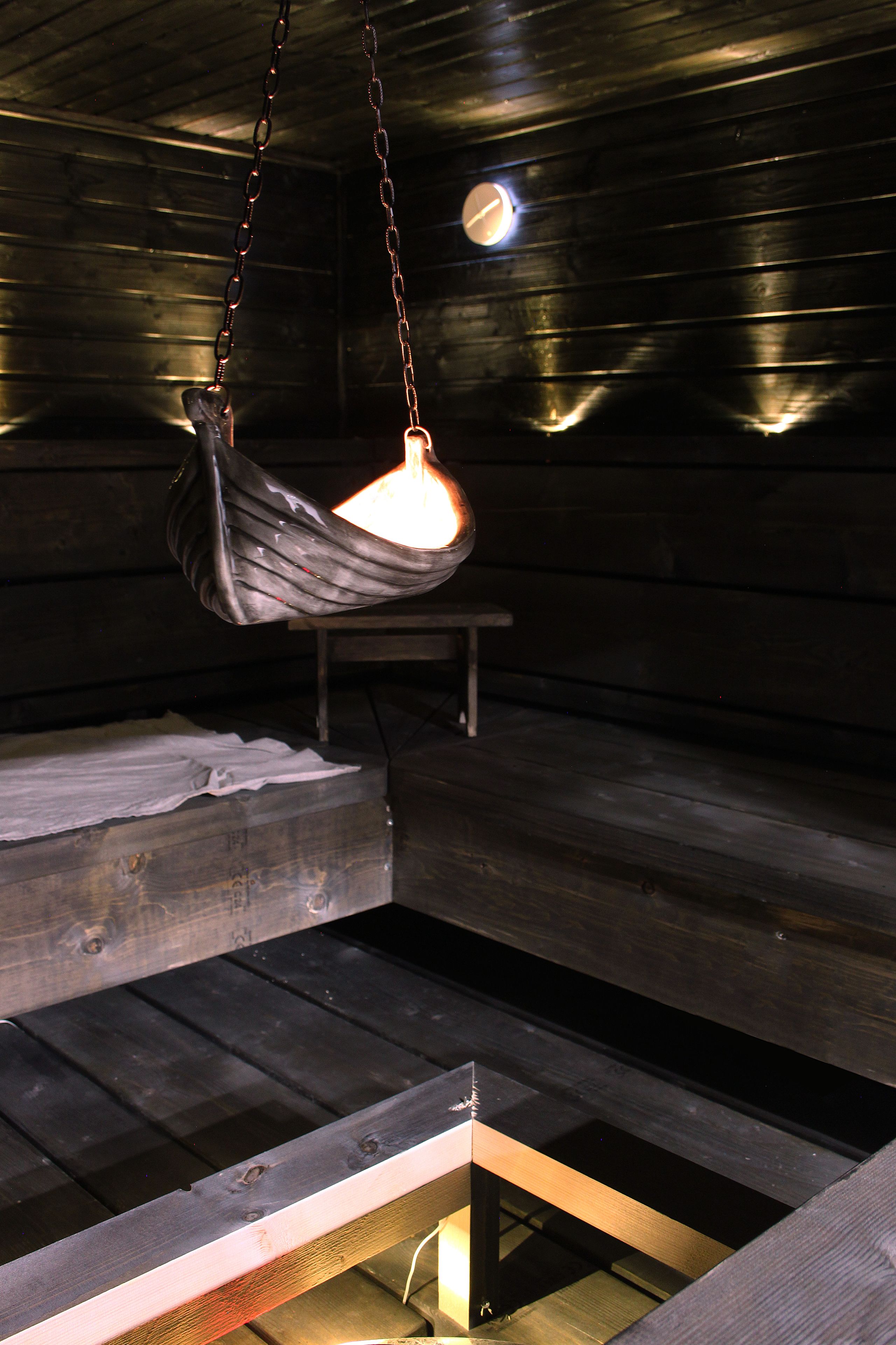 Interior de una cabaña de madera con una lámpara colgante y un banco.