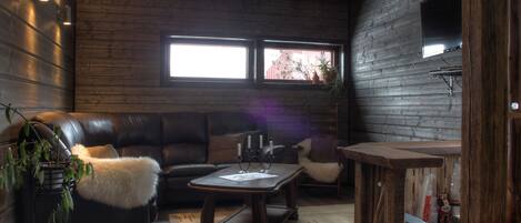 A cozy living room with a leather couch, a wooden coffee table, and a view through a window.