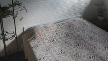 Una habitación con cama, un cuadro en la pared, una planta en maceta y un soporte metálico.