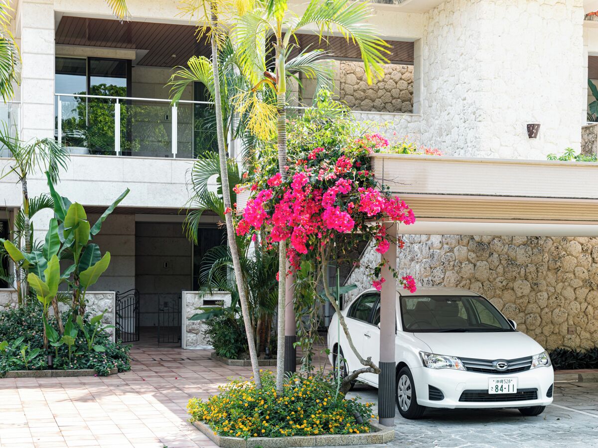 A white car parked in front of a building with a stone facade and a balcony.
