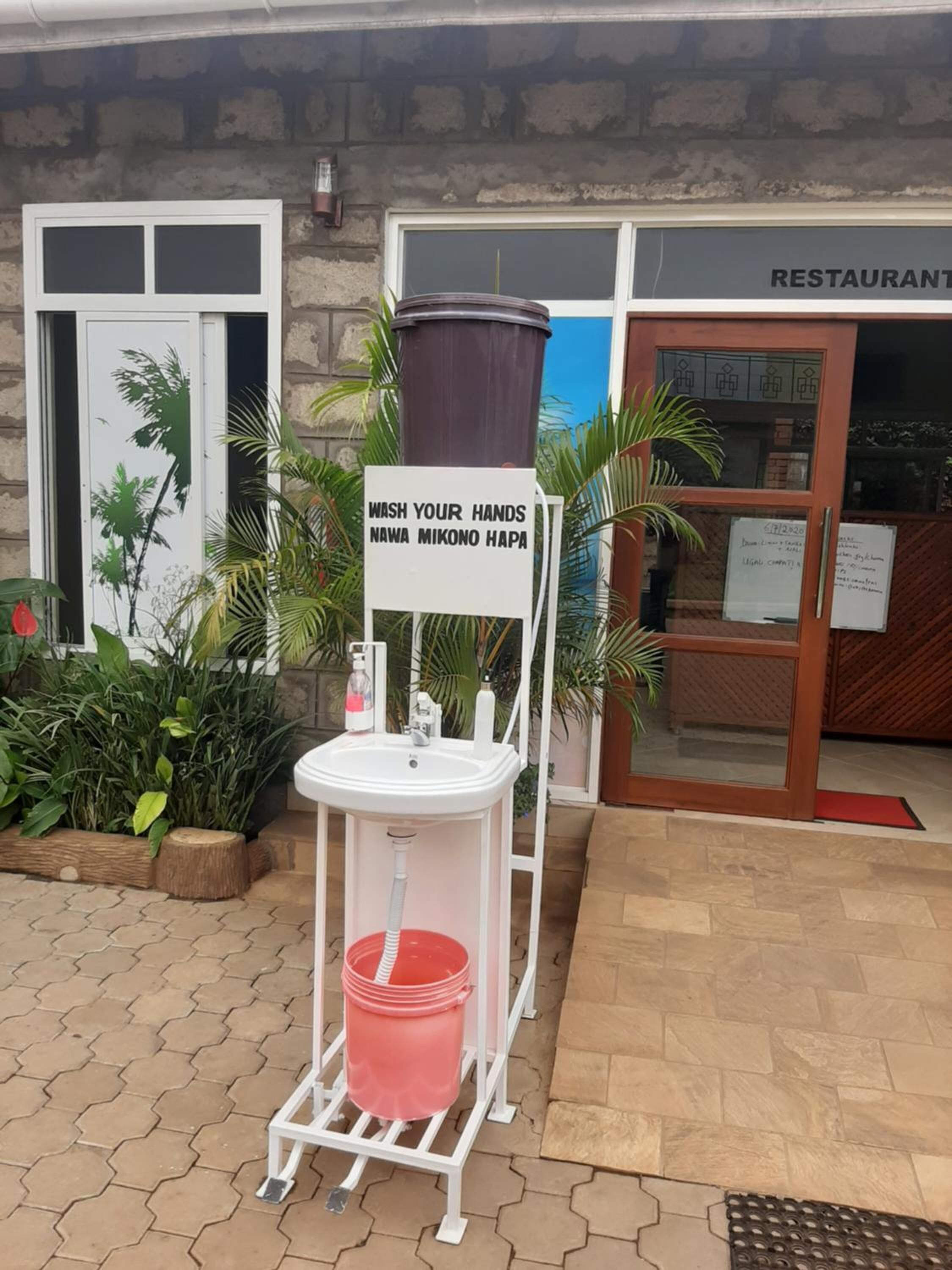 A handwashing station with a sign in English and another language, a red bucket, and a white sink.