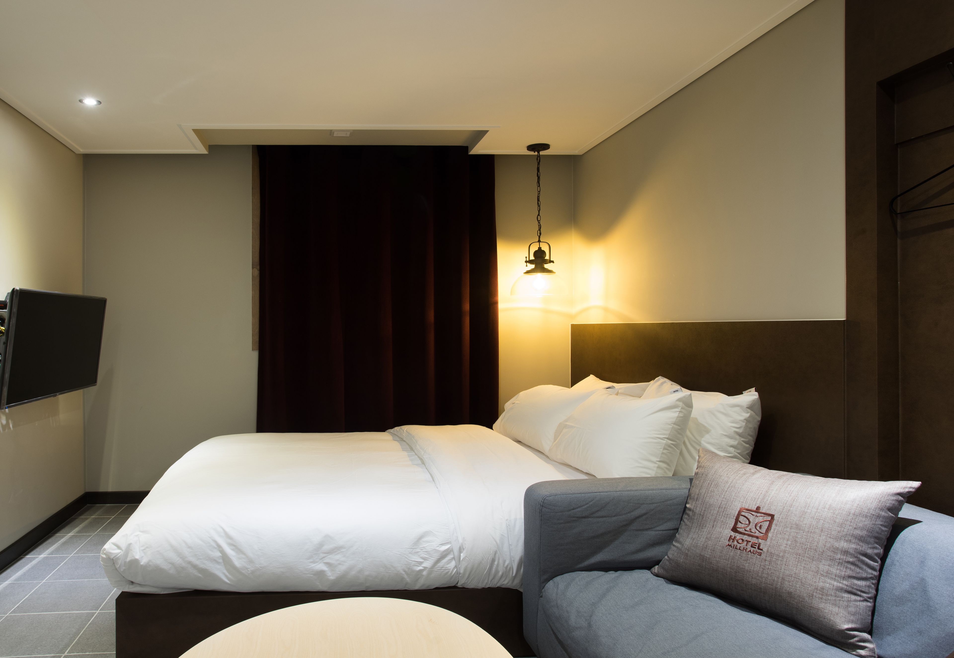 A hotel room with a bed, a sofa, a flat-screen TV, and a wall-mounted lamp.