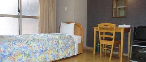 A hotel room with a bed, a desk, a chair, a television, and a window with curtains.