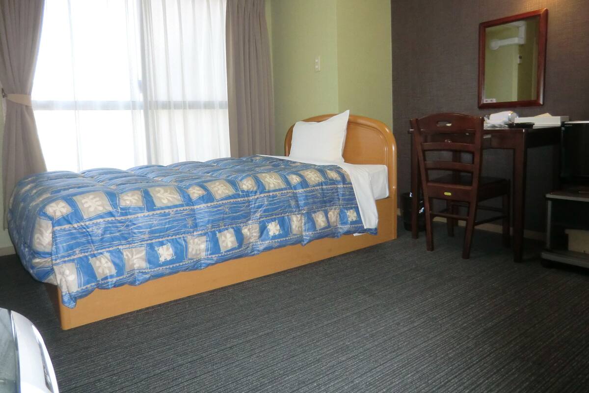 A hotel room with a bed, a desk, a chair, and a mirror.