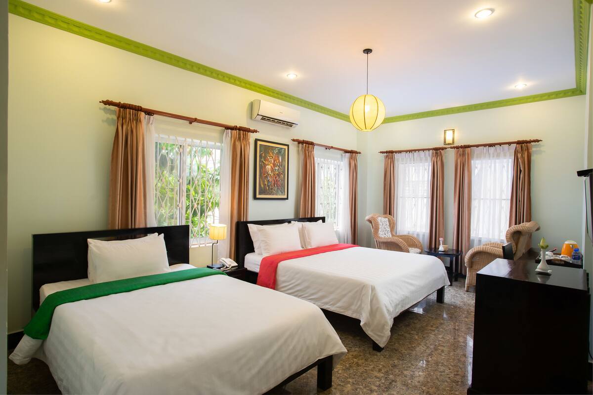 Habitación de hotel con dos camas, un escritorio, una silla y un ventanal con cortinas.