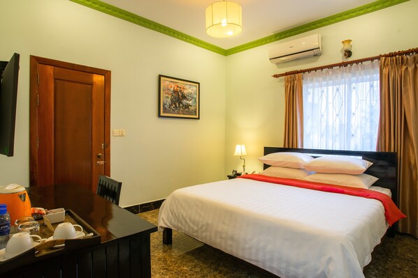 Une chambre d’hôtel avec un lit, un bureau sur lequel se trouve un plateau avec des articles pour le petit-déjeuner, un tableau au mur et un appareil de climatisation.