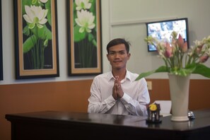 A reception desk with a vase of flowers, framed artwork on the wall, and a television screen in the background. - Han & Daniel Villa Boutique (Siem Reap)