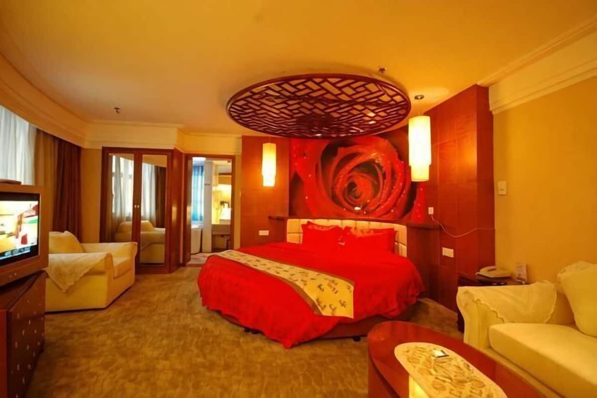 A hotel room with a large bed, a television, a sofa, and a decorative wall piece.