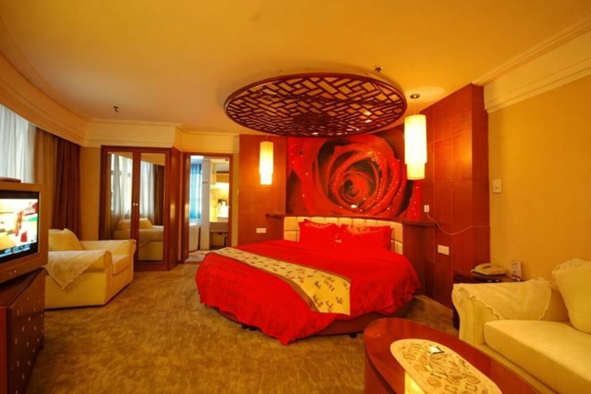 A hotel room with a large bed, a television, a sofa, and a decorative wall piece.
