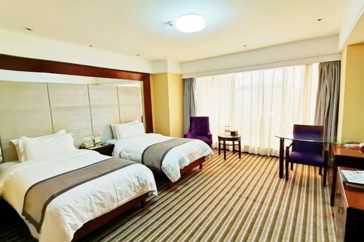 A hotel room with two beds, a desk, a chair, and a large window with curtains.