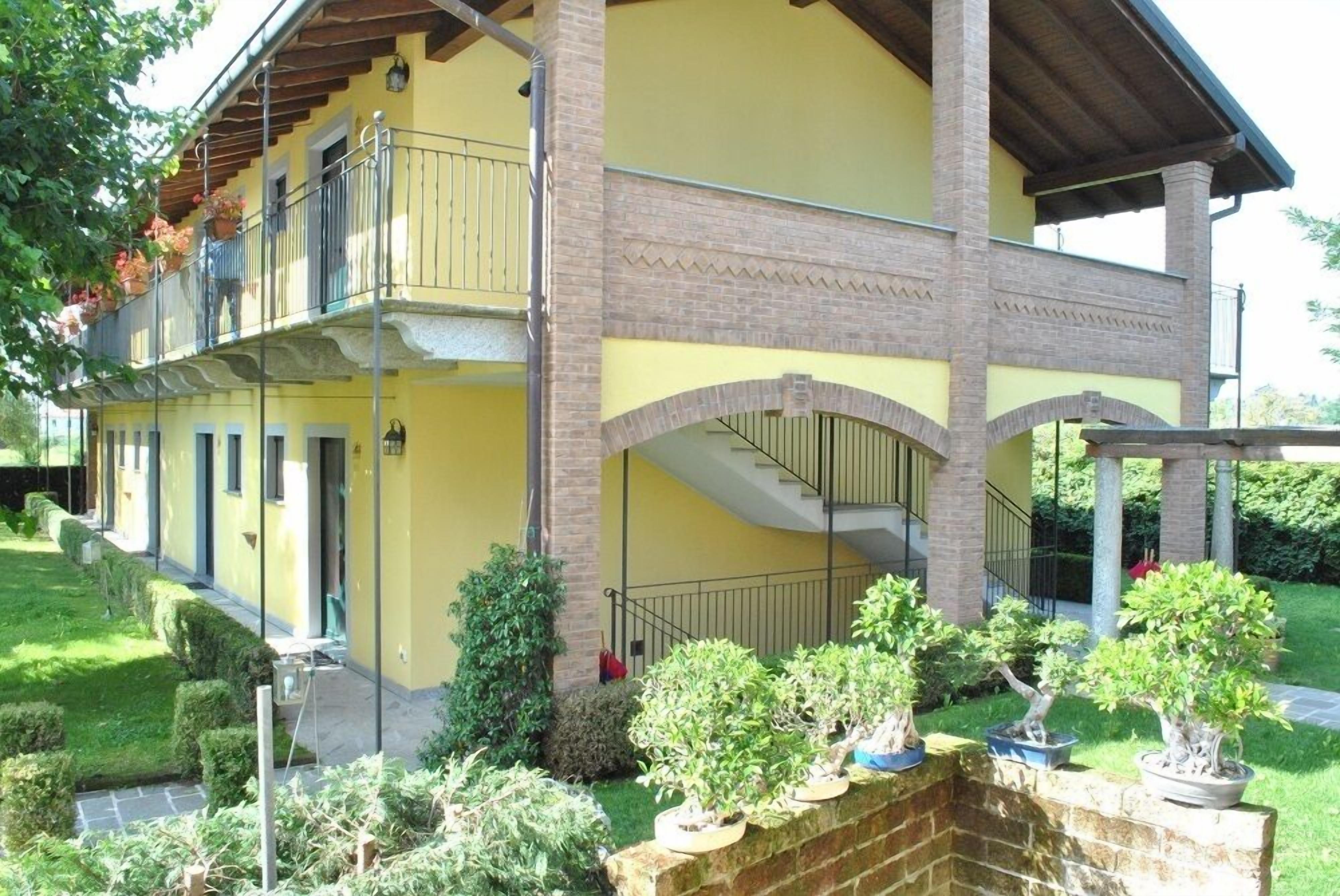 A two-story building with a yellow facade, a brick base, and a balcony with potted plants.