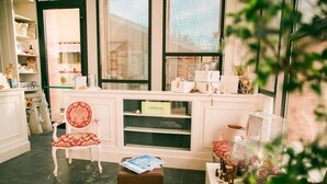 Un área de recepción con mostrador blanco, una silla tapizada en rojo, un reposapiés marrón y una ventana que ofrece vistas a un edificio de ladrillo.