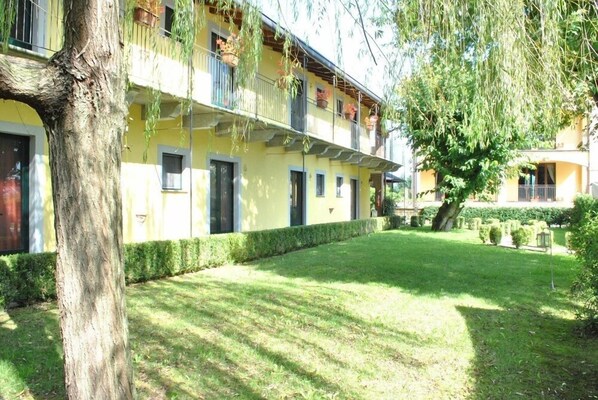 Um edifício amarelo com várias janelas e varandas, cercado por um gramado bem cuidado e árvores.