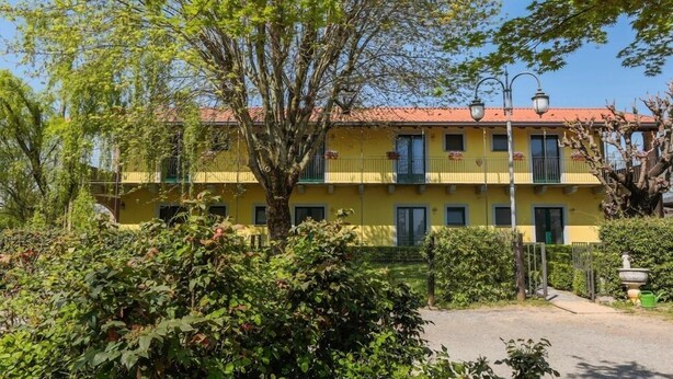 Un edificio amarillo de techo rojo, rodeado de vegetación y una pequeña fuente.