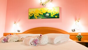 Habitación de hotel con cama, toallas, una botella y un cuadro de flores amarillas en la pared.