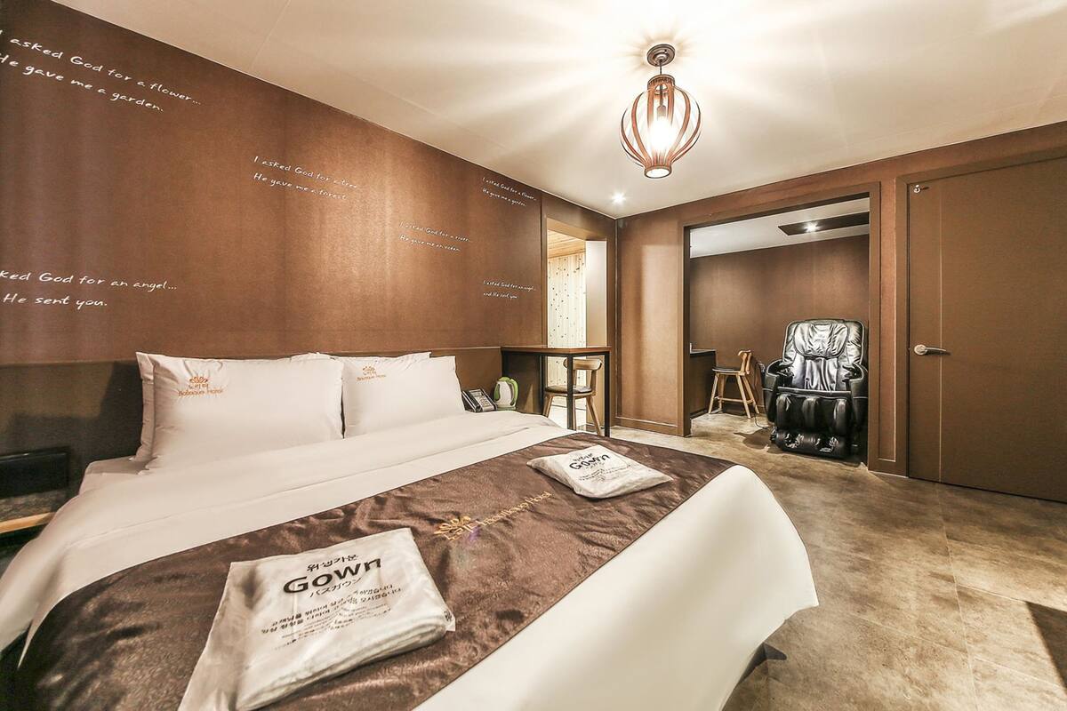 A hotel room with a large bed, a massage chair, a desk, and a wall with inspirational quotes.