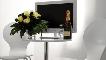 Una habitación moderna con un televisor blanco, un ramo de flores amarillas y una botella de champán.
