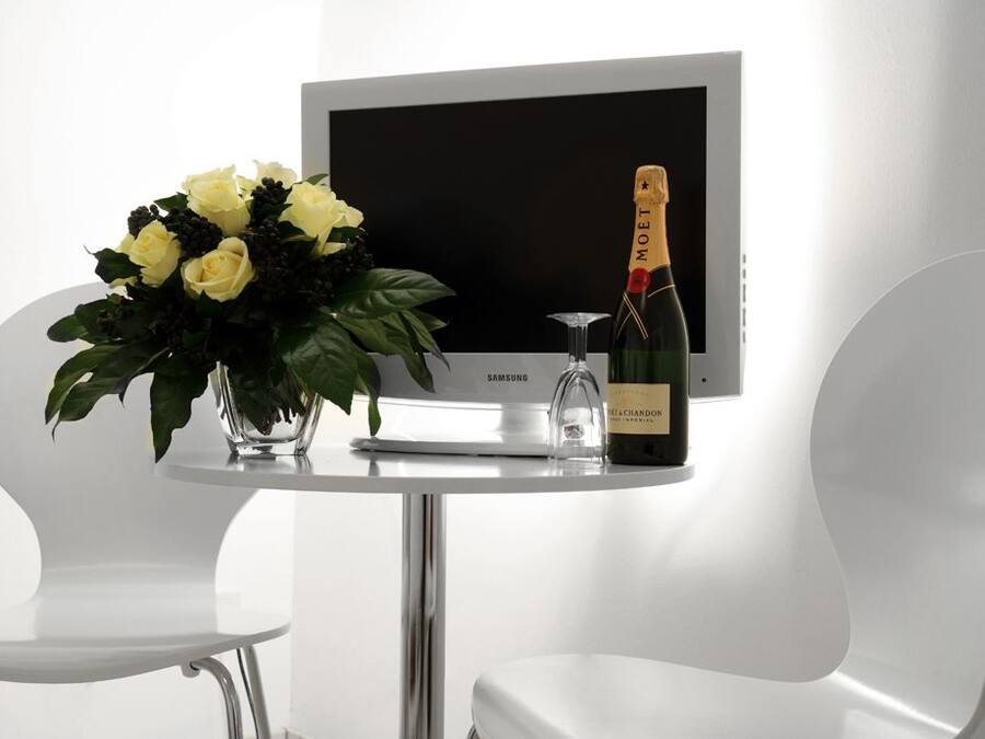 Una habitación moderna con un televisor blanco, un ramo de flores amarillas y una botella de champán.