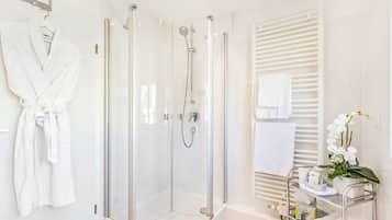 A modern bathroom with a glass-enclosed shower, a white robe hanging on the wall, and a vanity with a towel rack and a potted orchid.