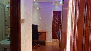 A hallway with wooden flooring, a desk with a chair, and a bathroom with a sink and toilet. - Fourways Junction VIP Suite (Nairobi)