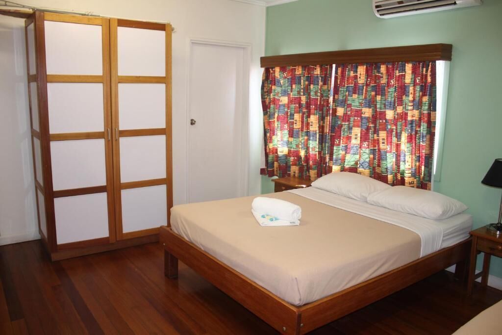 Un dormitorio con una cama de madera, una puerta blanca, una cortina colorida y una mesita de noche pequeña.