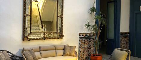 A spacious indoor area with a large ornate mirror, a beige sofa, two wicker chairs, and a small coffee table.