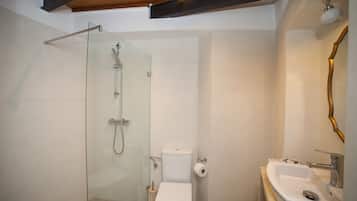 Un baño moderno con ducha envuelta en vidrio, inodoro blanco y lavamanos con grifo dorado.