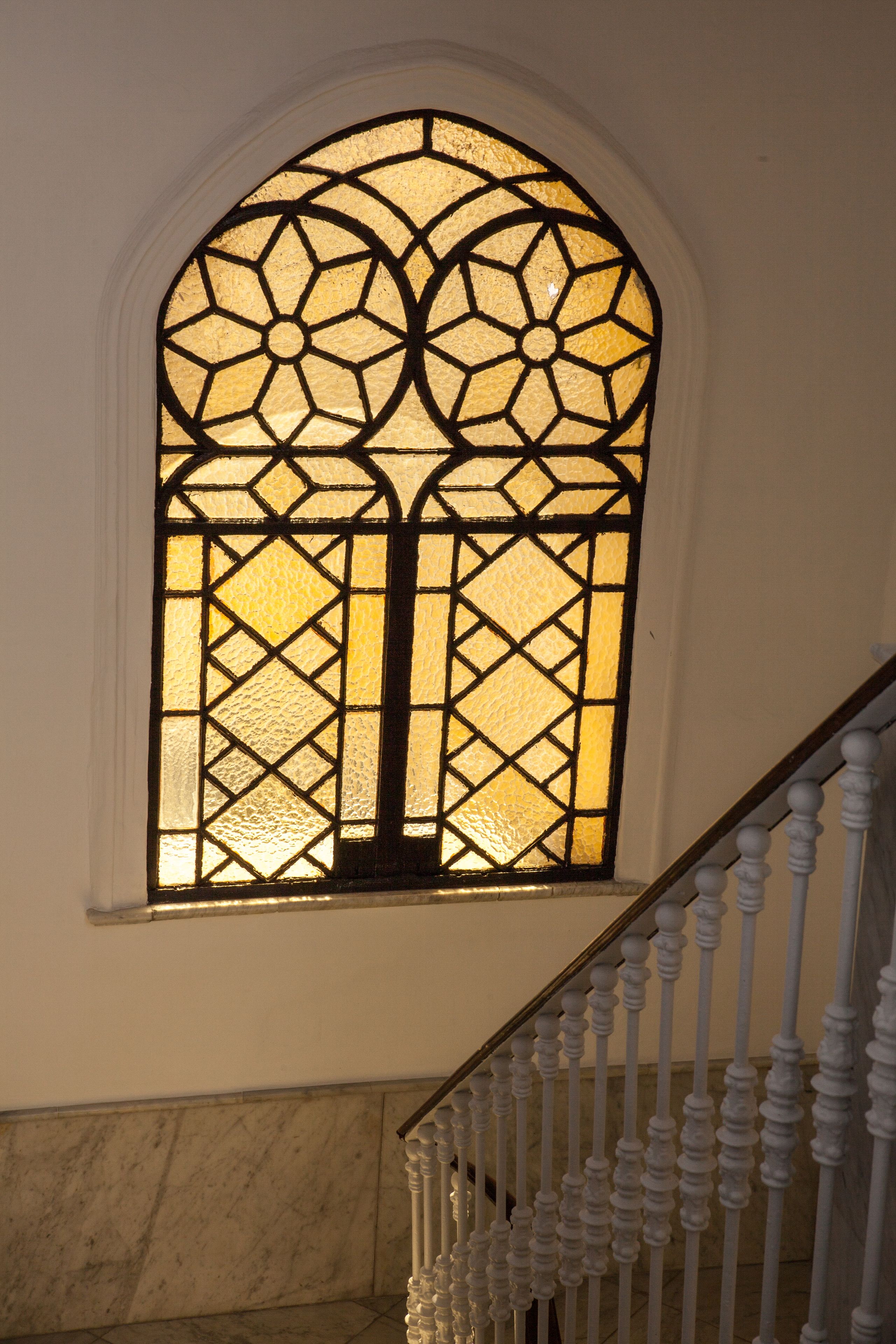 Una ventana de vitral con diseño geométrico, una pared de mármol y una barandilla blanca.