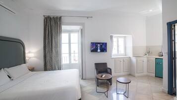 A hotel room with a bed, a desk, a chair, a TV, and a kitchenette.