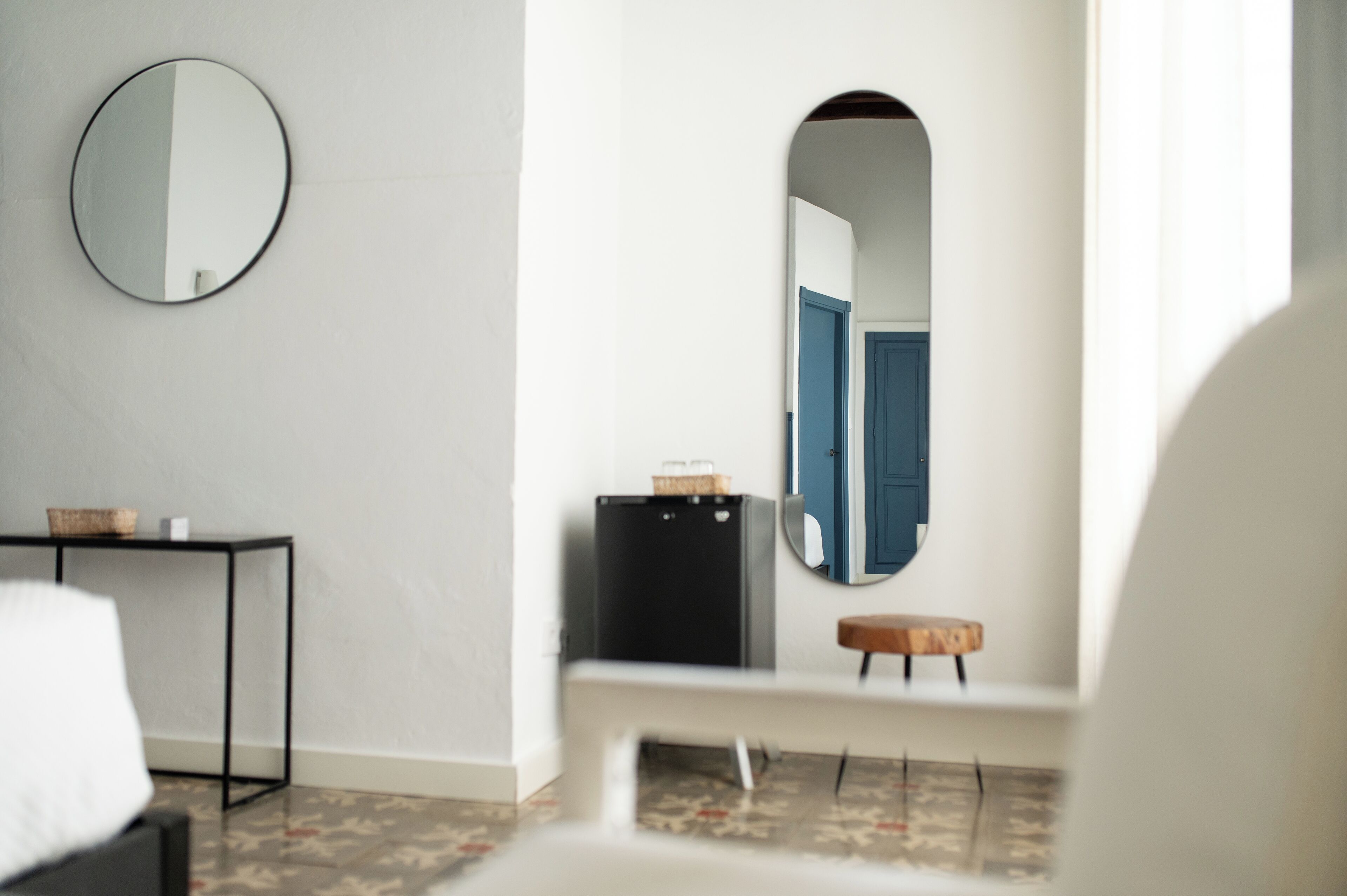 A modern room with a round mirror, a small table with a basket, a bench, and a door with a blue frame.