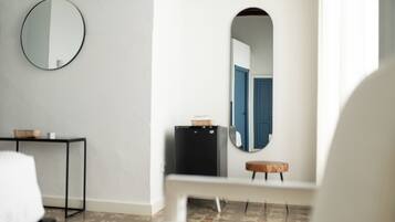 Een moderne kamer met een ronde spiegel, een klein tafeltje met een mand, een bankje en een deur met een blauwe omlijsting.