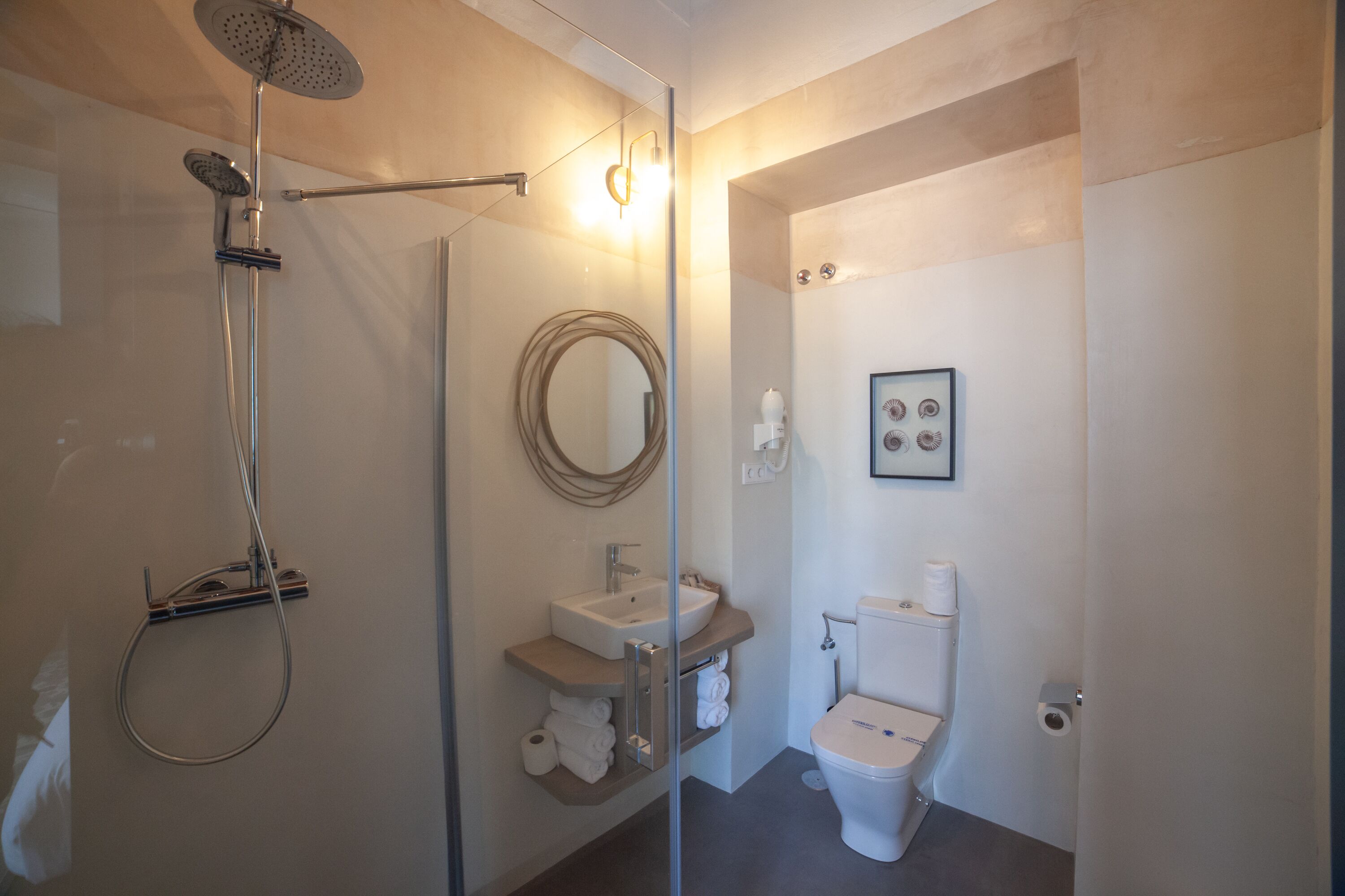 Un baño moderno con ducha vidriada, lavamanos, inodoro y un cuadro en la pared.
