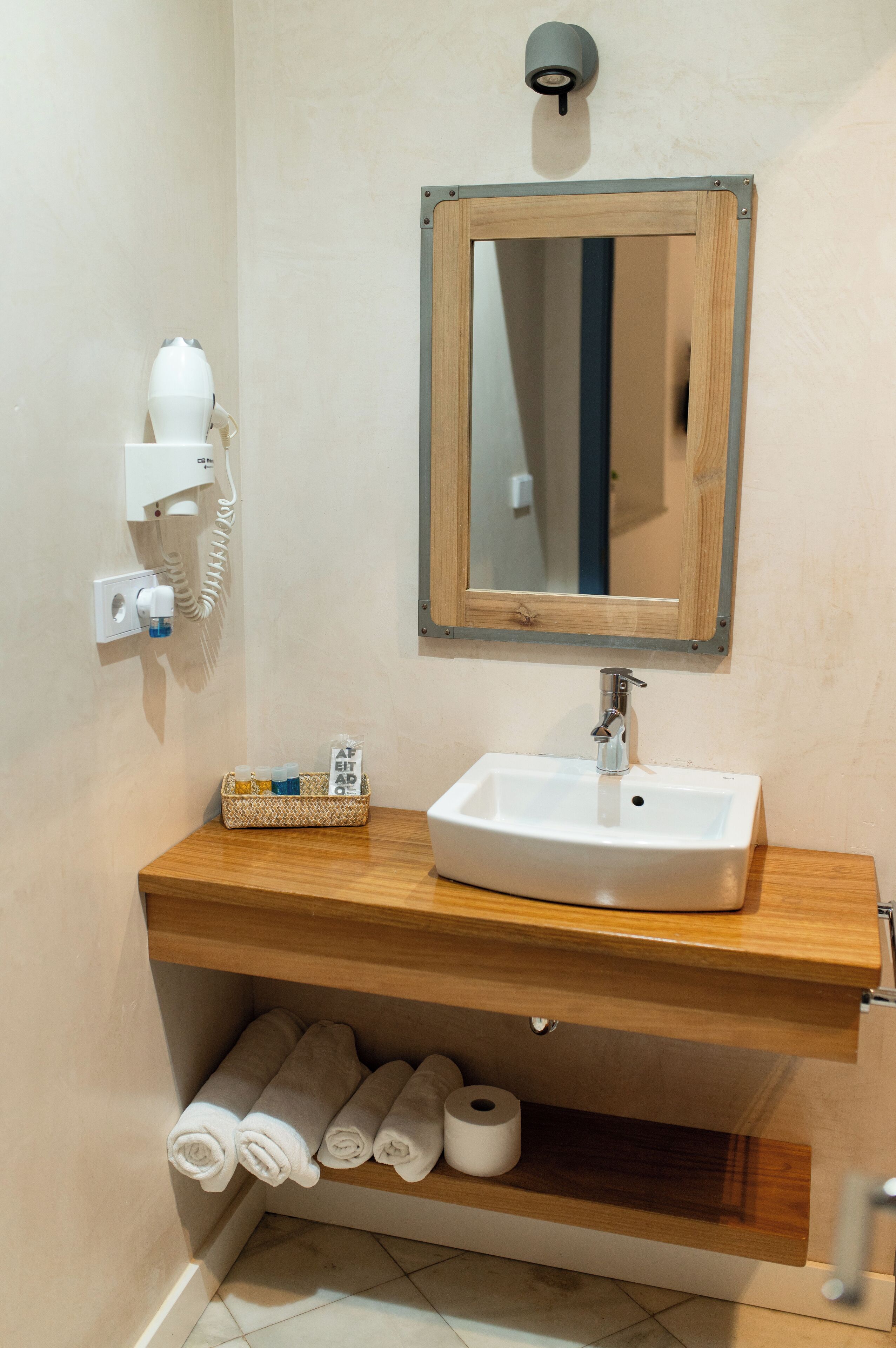 A bathroom with a wooden vanity, a white sink, a mirror, a towel rack, and a toilet paper holder.