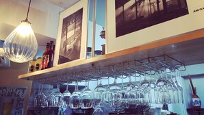 A bar area with a hanging light fixture, shelves with bottles, and a rack of wine glasses. - Douce (Ginowan)