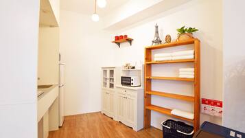 A compact kitchen with white cabinets, a microwave, and a small shelf with red containers.