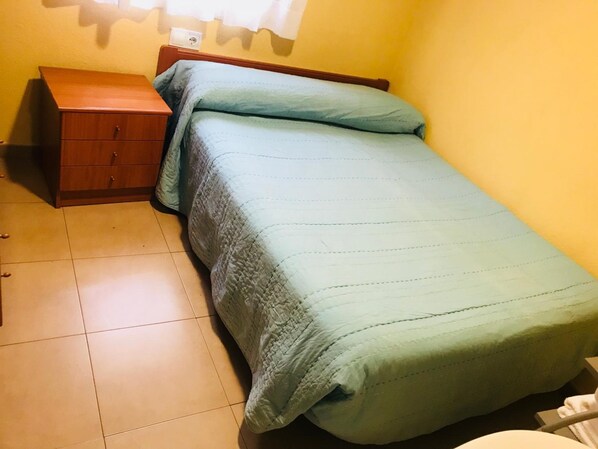 A small, neatly arranged bedroom with a single bed, a wooden nightstand, and a wall-mounted electrical outlet. - Pension la Estacion (Corvera de Asturias)