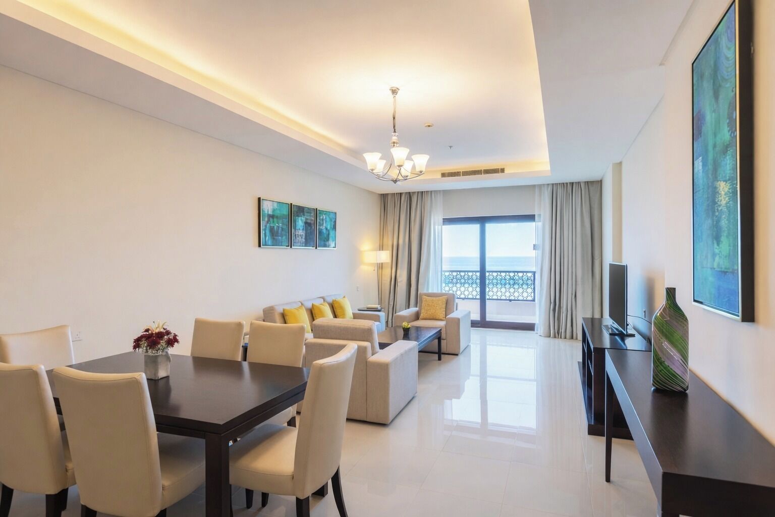 Een hotelkamer met een eethoek, een bank, een televisie en een balkon met uitzicht.