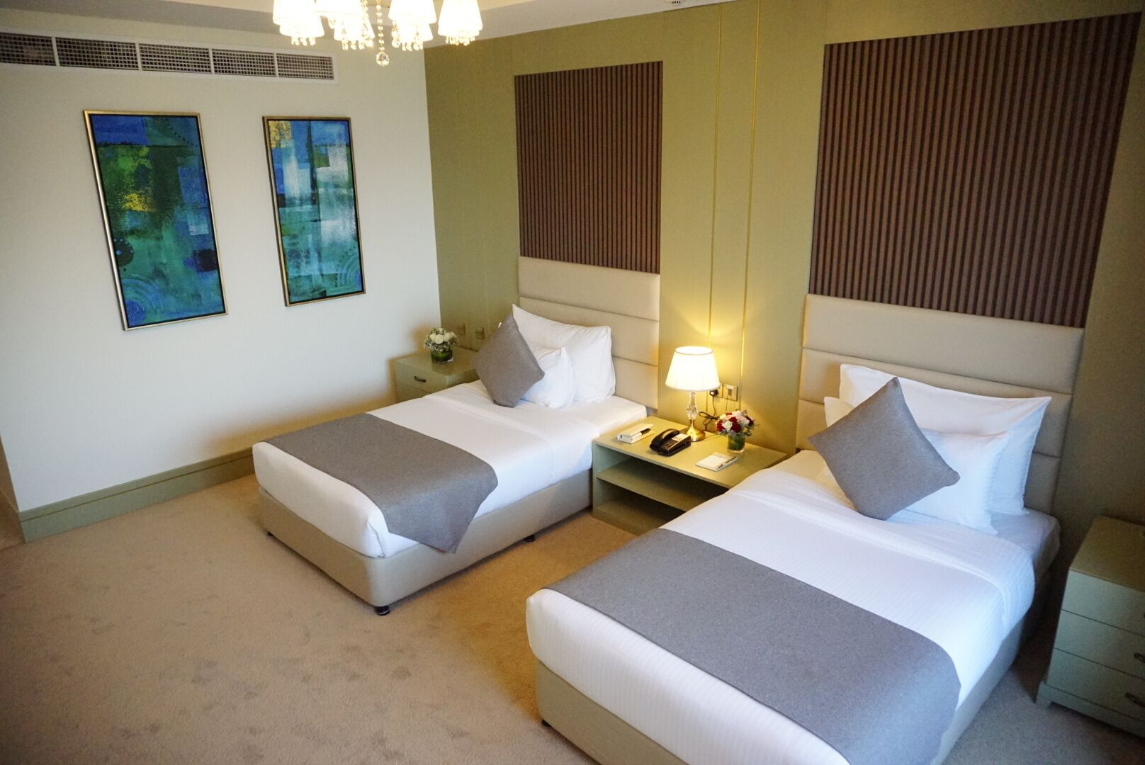 Een hotelkamer met twee bedden, een nachtkastje met een lamp, een telefoon en een vaas met bloemen.
