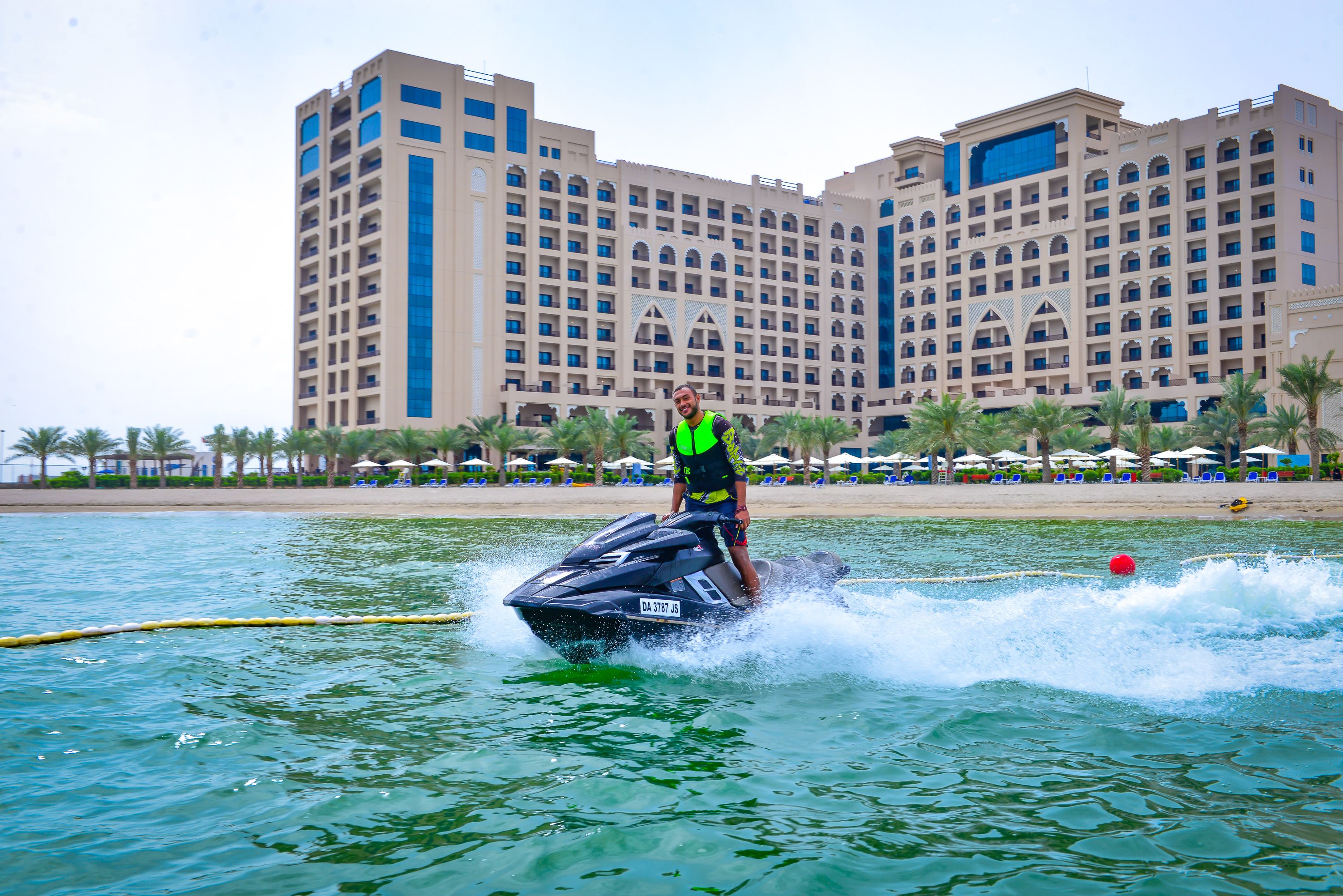 A person jet-skiing on a body of water with a large hotel in the background.