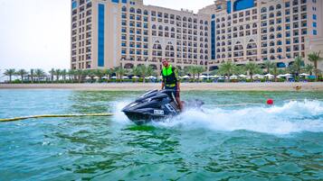A person jet-skiing on a body of water with a large hotel in the background.