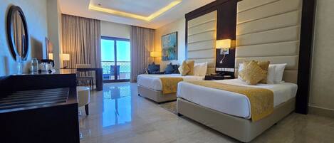 A hotel room with two beds, a desk, a chair, a balcony, and a large painting.