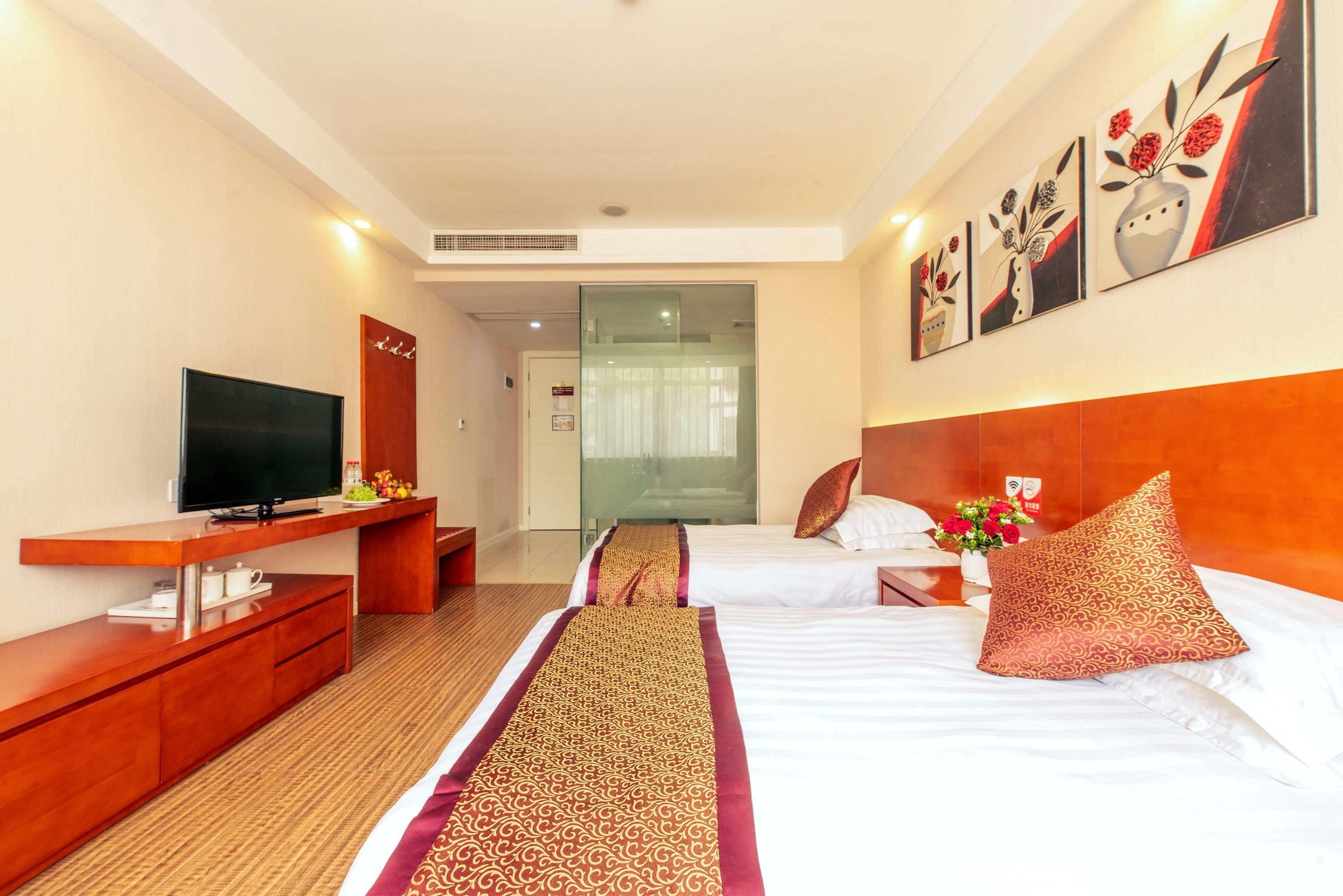 Habitación de hotel con televisor, muebles de madera, un corredor estampado y obras de arte en las paredes.
