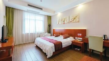 Ein Hotelzimmer mit einem großen Bett, einem Schreibtisch, einem Sessel, einem Fernseher und einem Fenster mit Vorhängen.