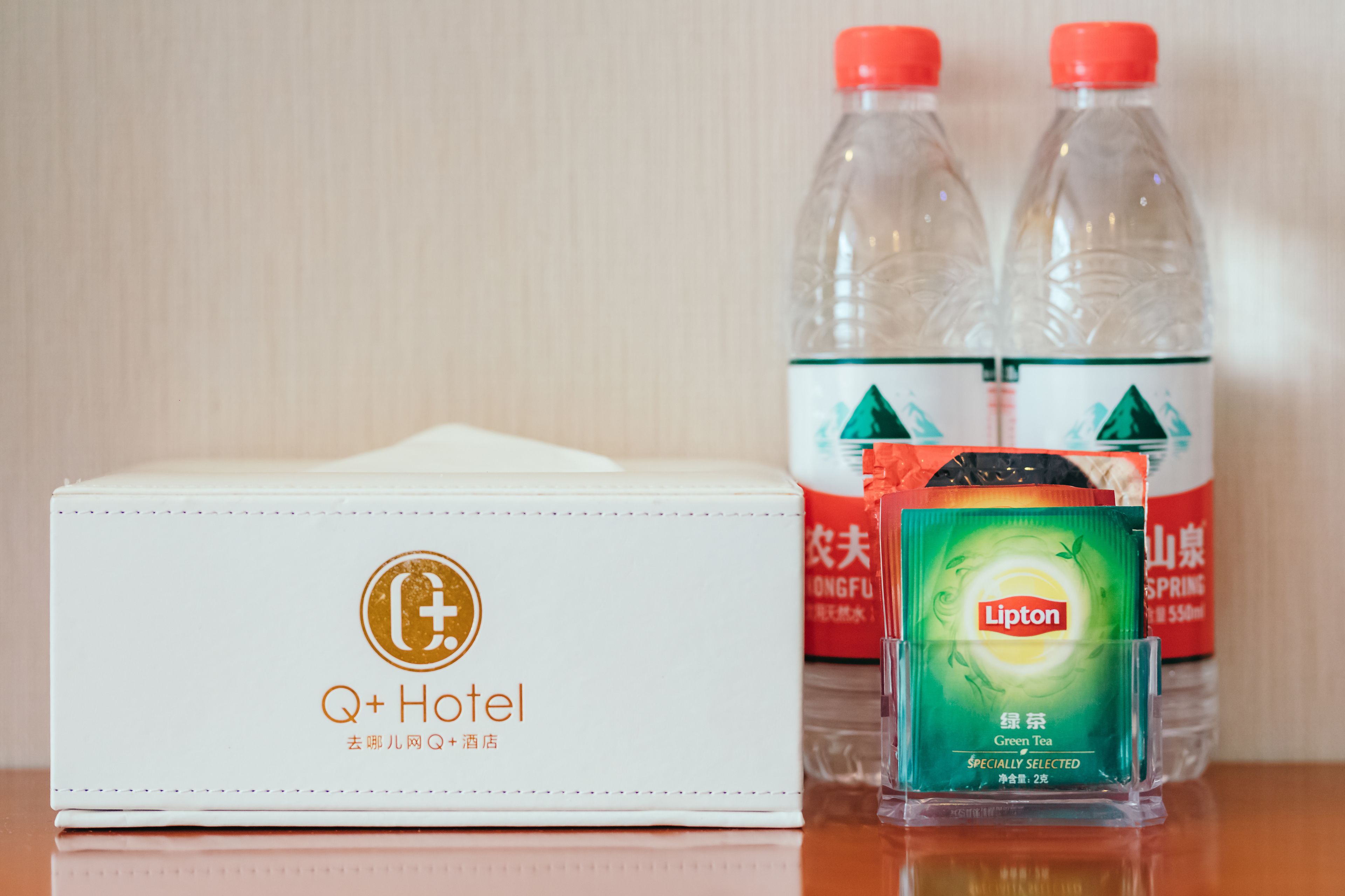 Una confezione a marchio Q+ Hotel, due bottiglie di tè verde Lipton e una bustina di tè verde Lipton.
