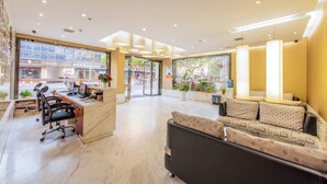 A hotel lobby with a reception desk, a sofa, and a large window offering a view of the street. - Xitang Hotel (Jiaxing)