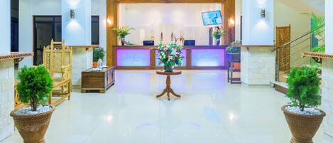 A hotel lobby with a reception desk, a staircase, and potted plants.