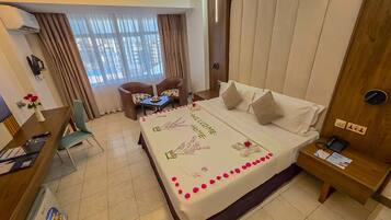 A hotel room with a bed, a desk, a chair, a small table, and a window with curtains.