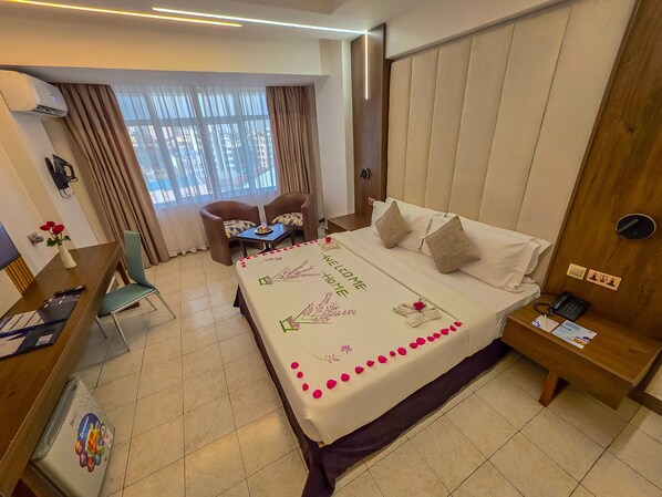 A hotel room with a bed, a desk, a chair, a small table, and a window with curtains.